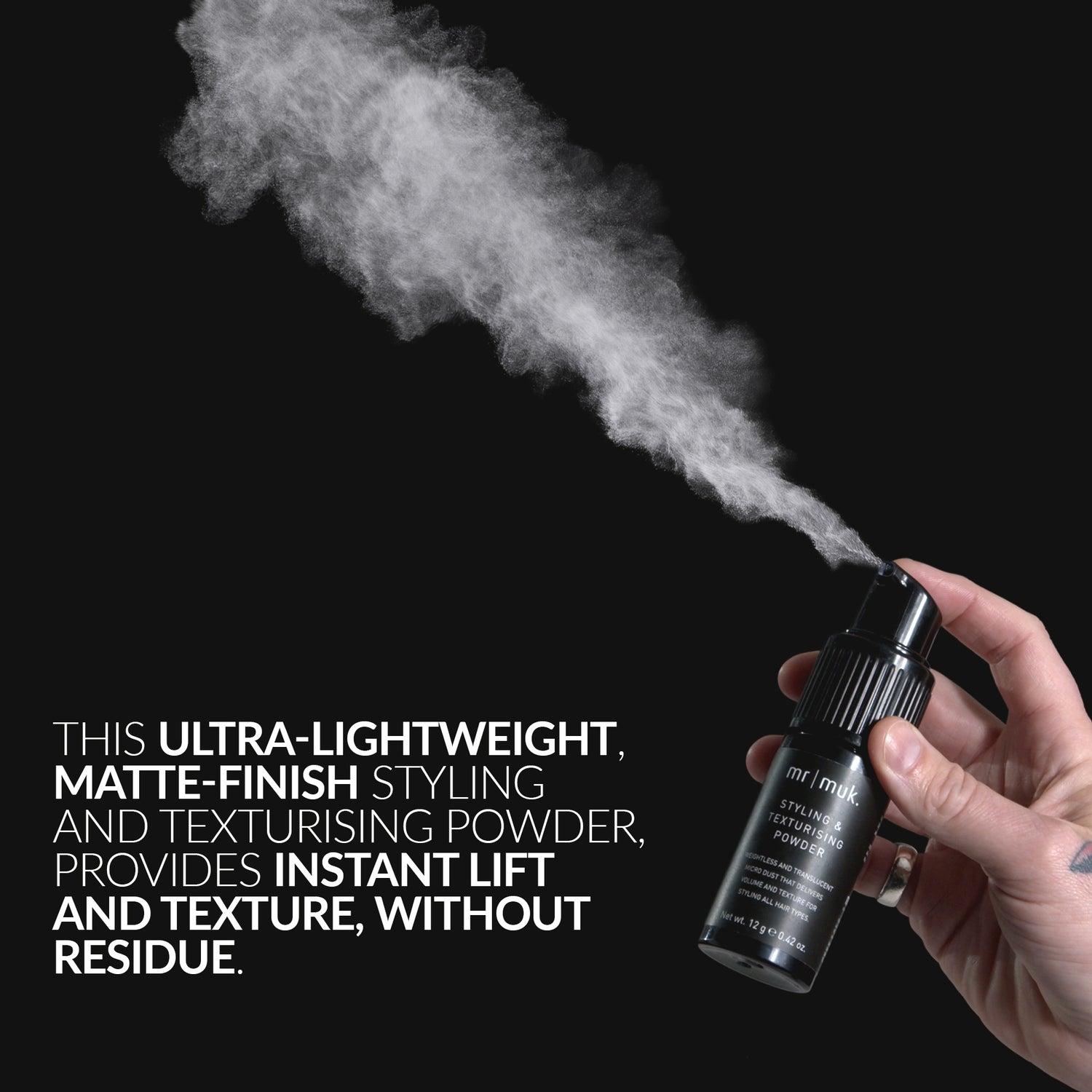 Hand holding a spray bottle with powder being released against a black background