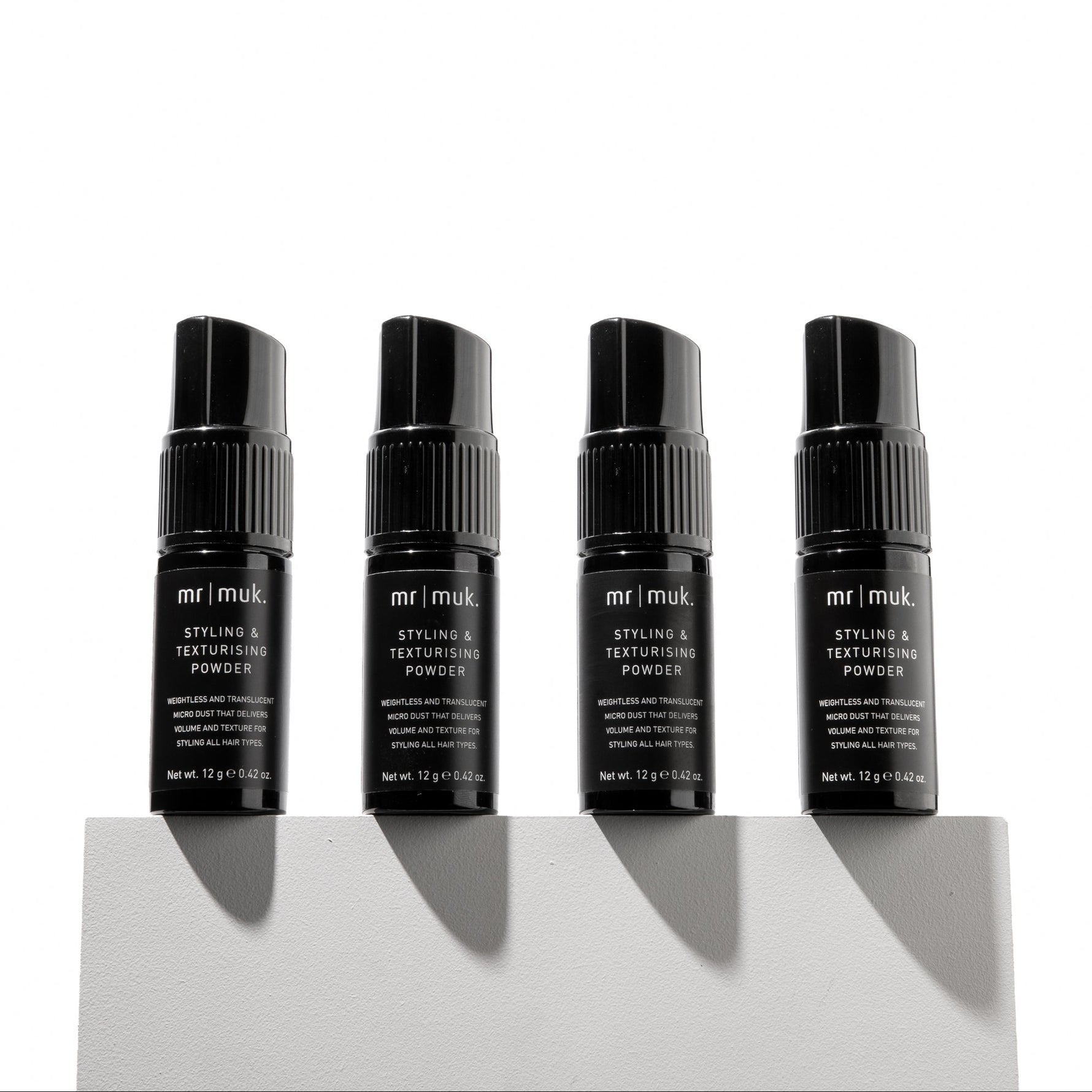 Four black bottles of Mr. Muk styling powder on a white background